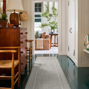 A gray woven indoor outdoor runner rug adds durable jute-look texture and easy-care style to a hallway or entryway with classic wood furniture, painted floors, and cozy home decor.